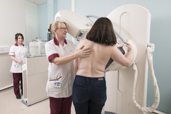 Woman undergoing a mammogram, supported by female healthcare professionals