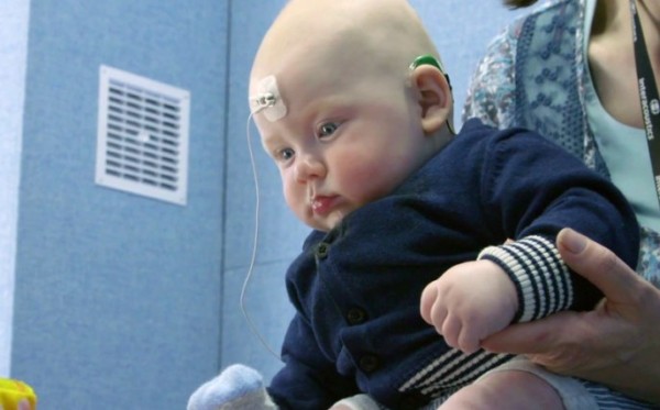 Baby with hearing aid undergoing a hearing test. Baby is being held by mother.