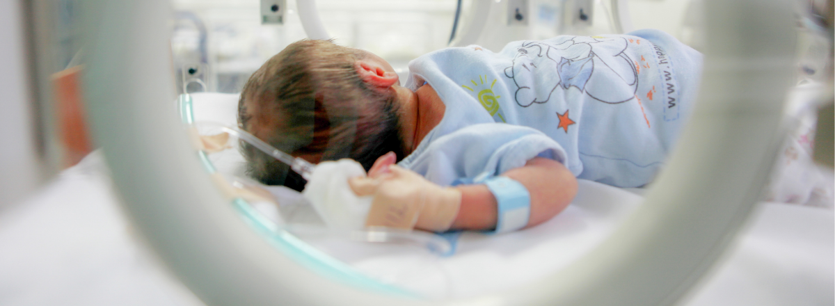 Image shows a newborn baby in a hospital incubator