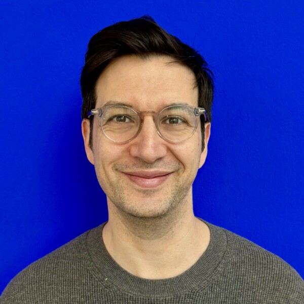 Dr Panos Sergouniotis wearing clear framed glasses and a grey jumper